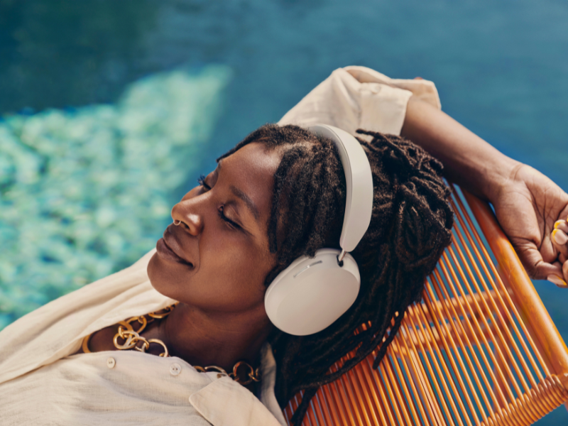 Vrouw ligt te zonnen in aan het zwembad en draagt de witte Sonos Ace koptelefoon